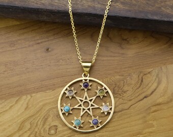 Può includere: Collana con pendente dorato con un design circolare, una stella centrale e scoppi di stelle, ognuno con una pietra preziosa di colore diverso. La collana è appesa a una delicata catena, su uno sfondo di legno.