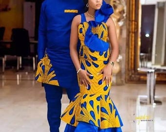 Op de afbeelding: Een stel in bijpassende outfits. De vrouw draagt een geel en blauw patroonjurk met een gelaagde rok. De man draagt een blauwe tuniek en broek met geel en blauwe patroonelementen. De outfits zijn formeel en waarschijnlijk voor een speciale gelegenheid.