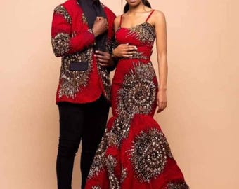 May include: A couple in matching red and gold patterned formal wear. The man wears a blazer over a black shirt and pants. The woman wears a spaghetti strap gown with a mermaid skirt. The outfits feature a circular design.