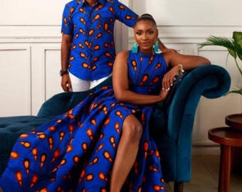 May include: A matching set of clothing featuring a blue fabric with orange feather-like patterns. The set includes a short-sleeved button-down shirt and a high-neckline dress with a thigh-high slit. The dress is worn with gold sandals.