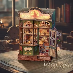 May include: A detailed miniature model of a magic shop, featuring a green and brown facade with arched windows and a sign that reads "Magic Shop." The shop's interior is visible, filled with tiny items. The model is on a table with a book.