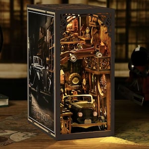 May include: A wooden book nook with a vintage car theme. The interior features a detailed diorama of a garage with miniature cars, tools, and car parts. The exterior has a black and white image of a street scene.