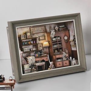 Peut inclure: Un diorama miniature encadré d'une mercerie, avec une machine à coudre, des étagères avec des bobines et un ours en peluche. Le cadre est gris et une machine à coudre miniature est devant le cadre.