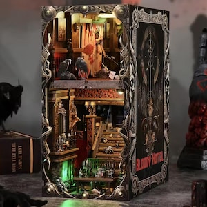 May include: A detailed, illuminated diorama of a haunted hotel, with intricate architectural details and a spooky atmosphere. The exterior is a book with the words "Bloody Hotel" on the spine. Includes a raven and a spider.