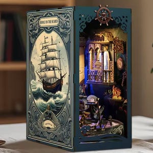 Peut inclure: Un diorama miniature détaillé et éclairé en forme de livre. Le livre ouvert révèle une scène nautique avec un voilier à gauche et une scène intérieure détaillée à droite. Le diorama est de couleur teal avec des motifs découpés.