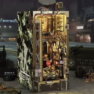 May include: A detailed military base model with a camouflage exterior. The interior features miniature tanks, shelves with equipment, and the text "Military Base" and "SWAT". The model has a stop sign and a radar dish.