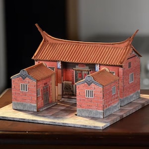 May include: A detailed paper model of an Asian temple. The model features a red brick facade, a tiled roof, and small side buildings. The model is set on a gray stone base.