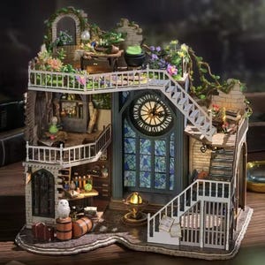 May include: A miniature dollhouse with a fantasy theme. The multi-level structure features a clock tower, a stained-glass window, and a staircase. The exterior is adorned with greenery and flowers. Interior details include a cauldron, owl, and laboratory equipment.