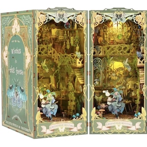 Puede incluir: Un diorama en miniatura detallado e iluminado que presenta una bruja en un entorno forestal. La caja es verde con detalles dorados y el texto "Witches in the Forest" y "Greenfield Mystery". El interior muestra una escena de varios niveles con hadas y setas.