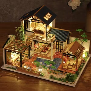 Peut inclure: Maquette de maison japonaise miniature avec plusieurs niveaux, ponts et un étang. Le modèle présente des espaces intérieurs détaillés, dont une chambre et une salle à manger, éclairés par de petites lumières. L'extérieur comprend des arbres miniatures et des aménagements paysagers.