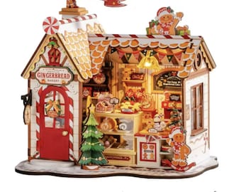 May include: A detailed miniature gingerbread bakery with a red door and orange roof. The sign reads "Gingerbread Bakery." A banner above says "Bringing Christmas Magic Home." The bakery is decorated with gingerbread men, a Christmas tree, and various festive treats.