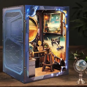 May include: A detailed, illuminated diorama of a futuristic space scene. The blue and silver exterior frames a room with a large planet, a telescope, and a painting of a space station. A small globe sits on a stand in the foreground.