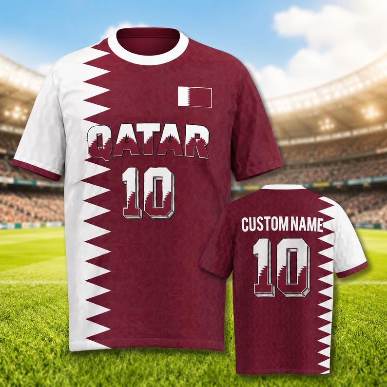 K&ouml;nnte beinhalten: Bordeaux-wei&szlig;es Fu&szlig;balltrikot mit dem Wort "QATAR" und der Nummer "10" auf der Vorderseite. Das Trikot hat ein wei&szlig;es Zickzack-Design an den Seiten und &Auml;rmeln. Ein zweites Trikot mit "CUSTOM NAME" und "10" ist ebenfalls zu sehen.