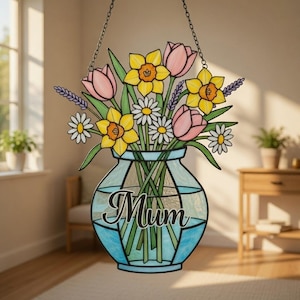Könnte beinhalten: Buntglas-Fensterdekoration mit einem Blumenstrauß in einer blauen Vase. Der Strauß enthält gelbe Narzissen, rosa Tulpen, weiße Gänseblümchen und lila Lavendel. Das Wort "Mum" ist auf der Vase geschrieben.