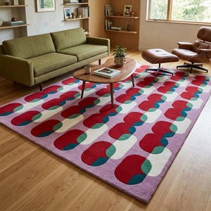 May include: A rectangular area rug featuring a repeating geometric pattern of interlocking rounded shapes in shades of red, teal, and off-white, set against a light purple background, covering a portion of a wooden floor in a living room.