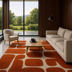 May include: A contemporary living room with an orange and cream patterned rug. The rug has a geometric design of rounded rectangles. The room also features a beige sofa, armchair, wooden coffee table, and a large window with a view of a green landscape.