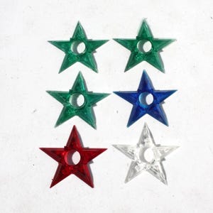 May include: Six star-shaped Christmas light covers in various colors: green, blue, red, and clear. Each star has a hole in the center for a light bulb. The covers are made of a translucent material.