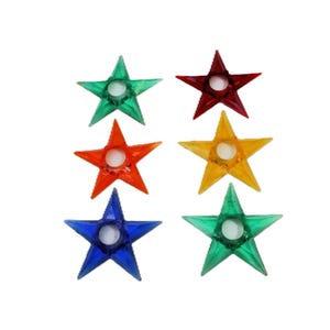 May include: Six colorful star-shaped candle holders in green, red, orange, yellow, blue, and another green. Each star has a circular indentation in the center for a candle. The candle holders are made of a translucent material.
