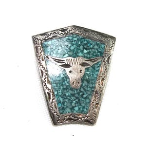 May include: A silver-toned, shield-shaped pendant with a turquoise inlay and a bull's head design. The pendant has a decorative border and a detailed bull's head in the center, showcasing a Southwestern or Western theme.