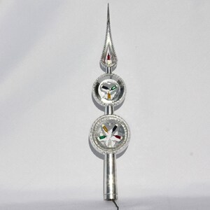 May include: Silver Christmas tree topper with a pointed top and three circular sections. The sections have a white background with colorful accents. The top section has a red and white accent, the middle section has a green, white, and gold accent, and the bottom section has a green, white, and black accent.