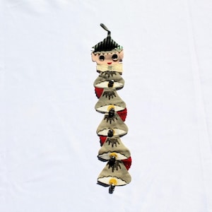 May include: A vintage Christmas decoration featuring a felt elf with a green and white striped hat, a red bow tie, and a series of five felt bells with gold glitter and red trim.