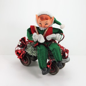 May include: A green and red elf doll riding a toy wagon decorated with red bells and green tinsel.