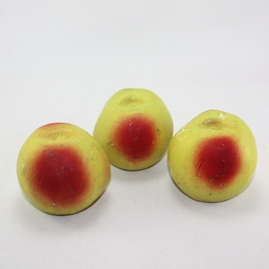 May include: Three artificial fruit, each with a yellow exterior and a red center, resembling peaches.