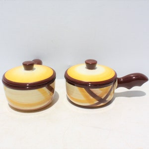 May include: Two small ceramic pots with brown handles and lids. The pots are decorated with a yellow and brown geometric pattern.