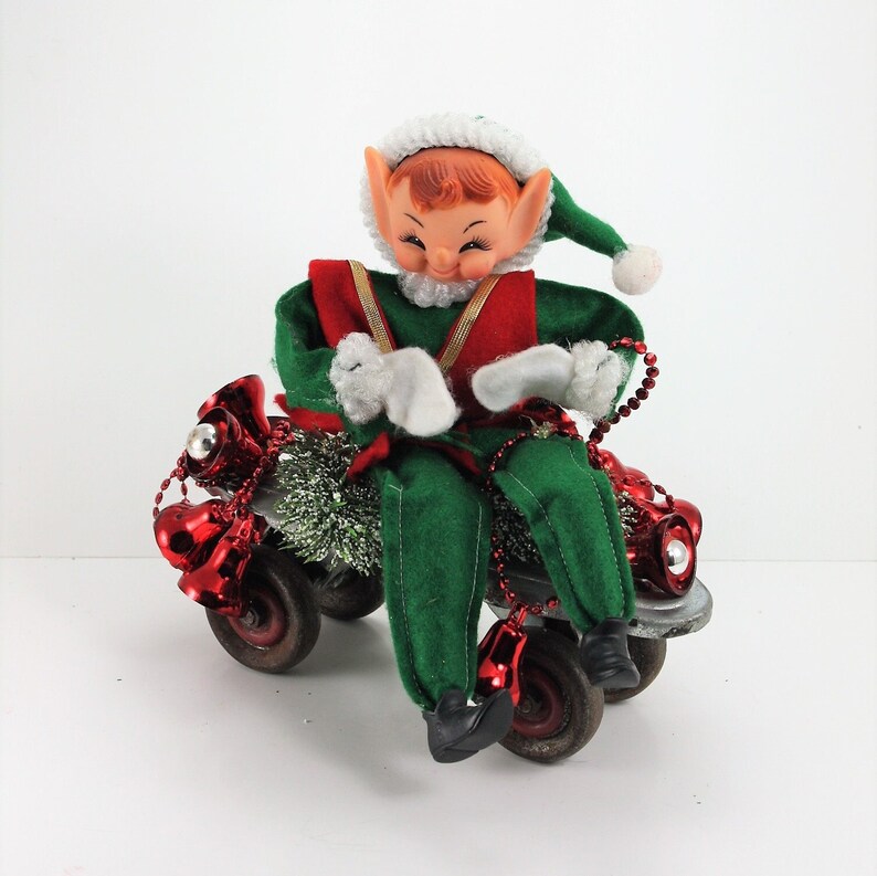 May include: A green and red elf doll riding a toy wagon decorated with red bells and green tinsel.