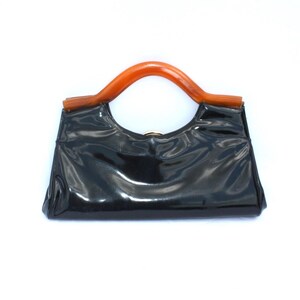 May include: A glossy black handbag with a curved, orange-brown handle. The bag has a rectangular shape with a slight curve at the top. The handle is made of a smooth, possibly plastic material, and is attached to the bag with gold-colored hardware.