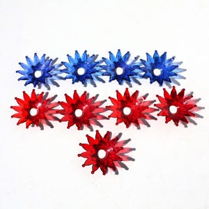 May include: A collection of star-shaped Christmas light covers in red and blue. The covers are arranged in rows, with a white center hole. The plastic covers cast a shadow on the white surface.