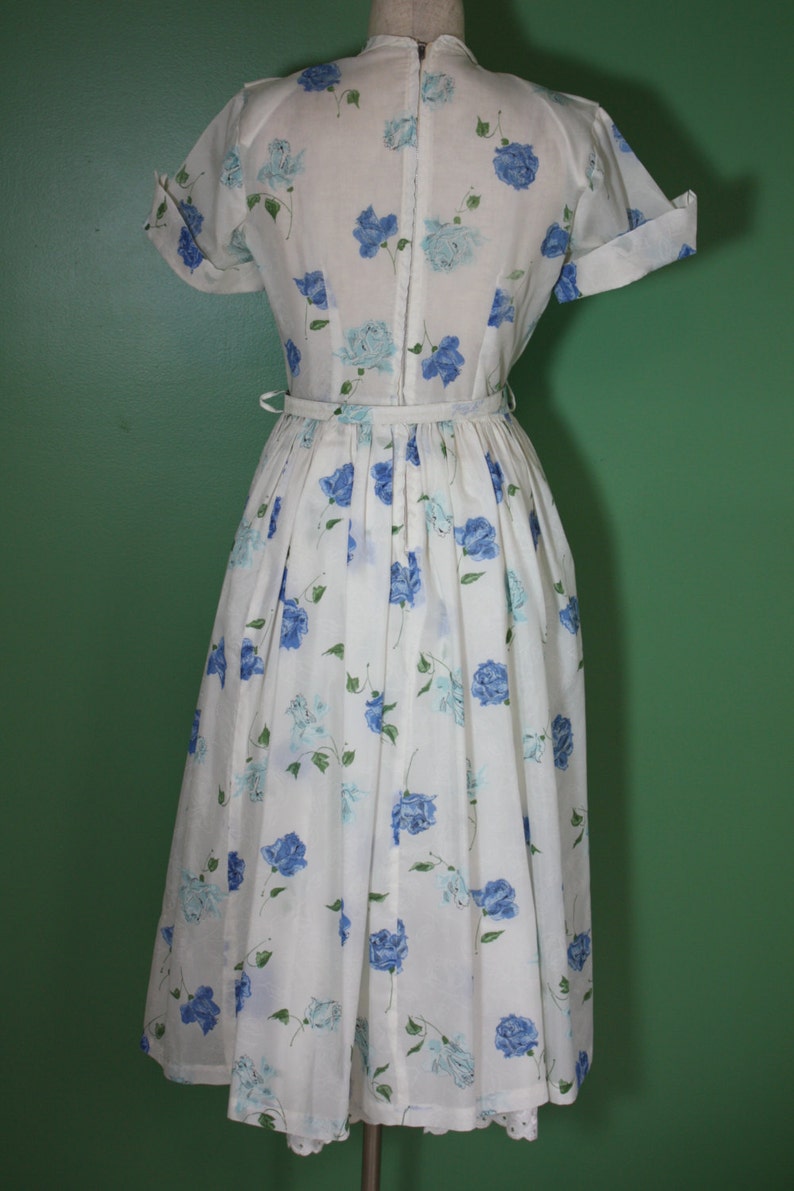 May include: A white dress with a blue floral print and a back zipper closure. The dress has short sleeves and a full skirt.