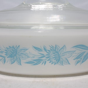 May include: A white casserole dish with a clear glass lid. The dish features a floral design in light blue. The flowers and leaves are arranged in a horizontal pattern around the dish.