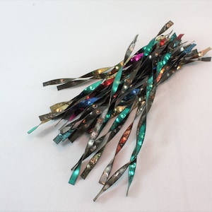 May include: A cluster of metallic, twisted ribbons in shades of green, silver, and bronze. The ribbons have a reflective, iridescent quality, with hints of red, blue, and gold. The ends are cut at an angle, and the overall effect is decorative.