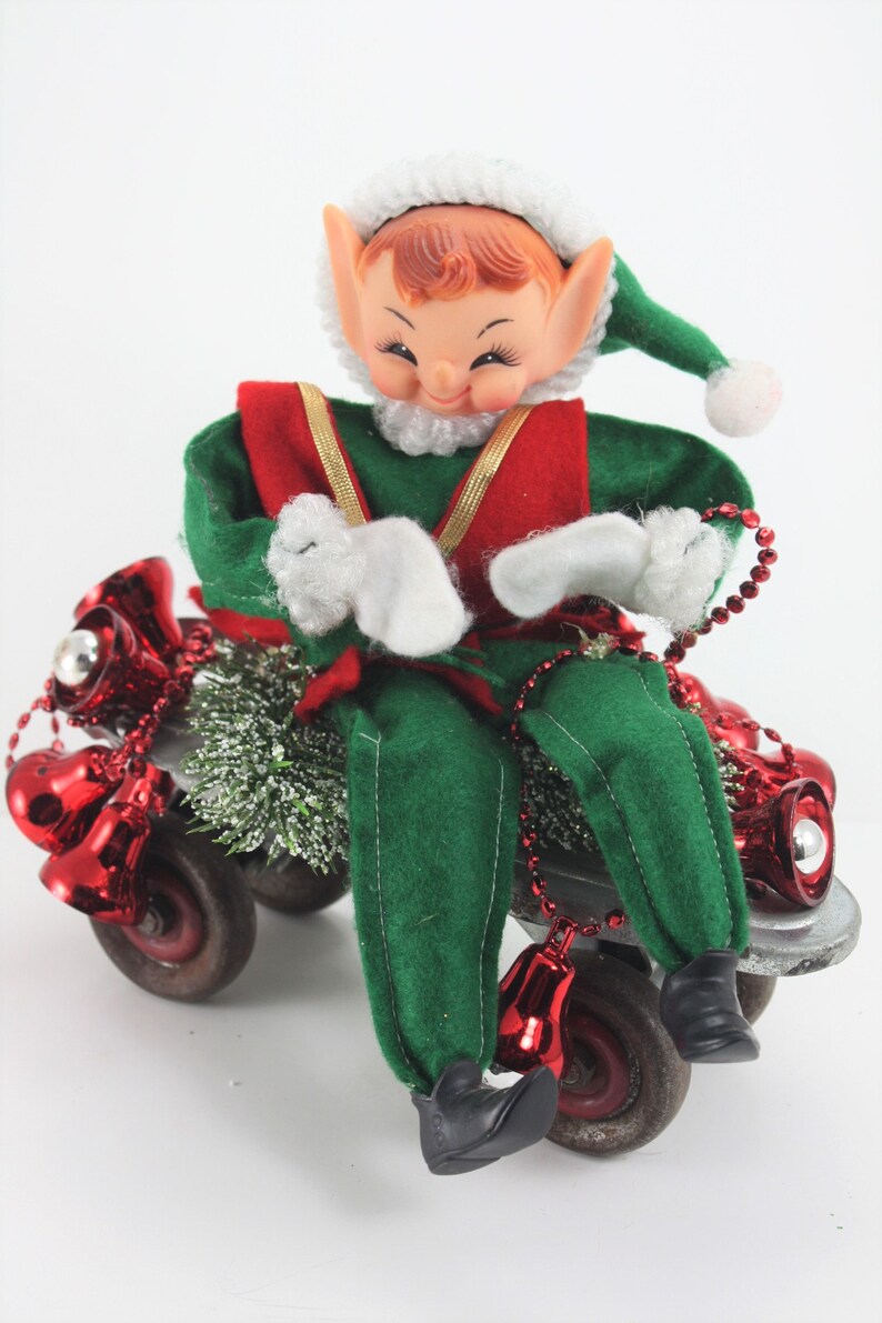 May include: A green and red elf doll riding a toy skateboard decorated with red jingle bells and green tinsel.