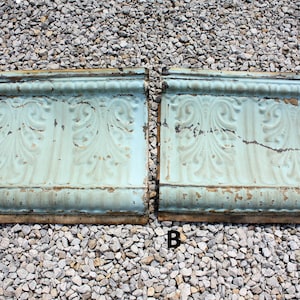 May include: Two antique, light blue, metal ceiling tiles with a decorative, embossed floral pattern. The tiles are slightly curved and have a distressed, aged look.
