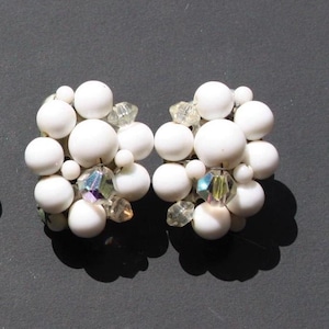May include: A pair of white cluster earrings with iridescent crystal accents. The earrings are made of white beads and crystals.