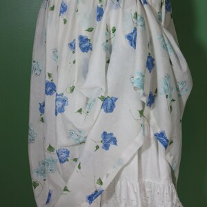 May include: A white dress with a blue floral print and a white lace trim. The dress has a gathered skirt and a belt.