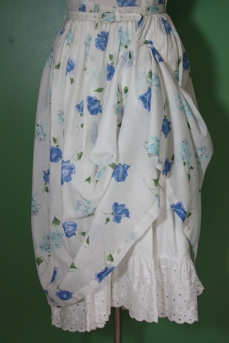 May include: A white dress with a blue floral print and a white lace trim. The dress has a gathered skirt and a belt.