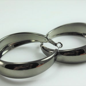 May include: A pair of large, hoop earrings with a shiny, gunmetal finish.