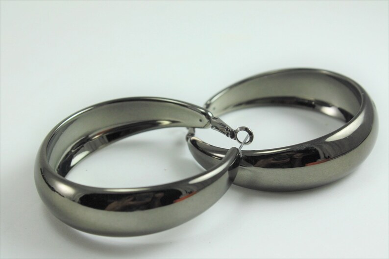 May include: A pair of large, hoop earrings with a shiny, gunmetal finish.