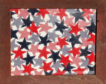 May include: A framed artwork featuring a repeating pattern of red and black stars on a white background. The stars are outlined in black and have a stitched appearance.