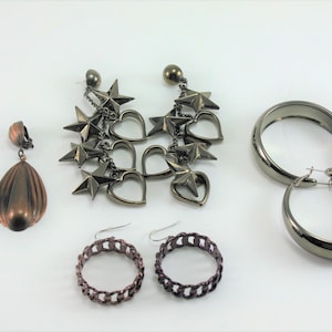 May include: Five pairs of earrings in various styles. Two pairs are copper-colored and have a teardrop shape. One pair is silver-toned and features a dangling chain with stars and hearts. The other two pairs are silver-toned hoops, one pair is thick and the other is a chain link style.