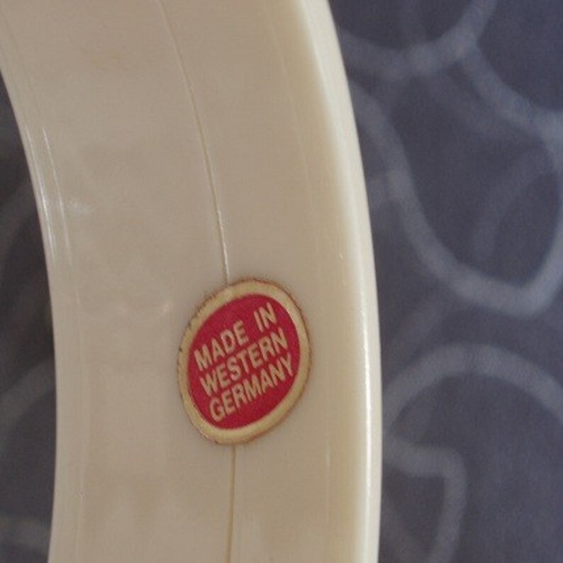 Pu&ograve; includere: Un anello di plastica bianco con un adesivo rosso che dice "Made in Western Germany".