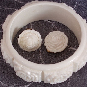 Pu&ograve; includere: Braccialetto bianco in plastica con un design a rosa scolpita. Il braccialetto &egrave; decorato con due orecchini in plastica bianca a forma di rosa.
