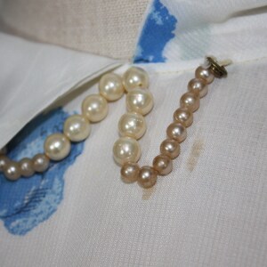 May include: A white blouse with a blue floral pattern and a white collar. A pearl necklace is attached to the collar with a small metal clasp.