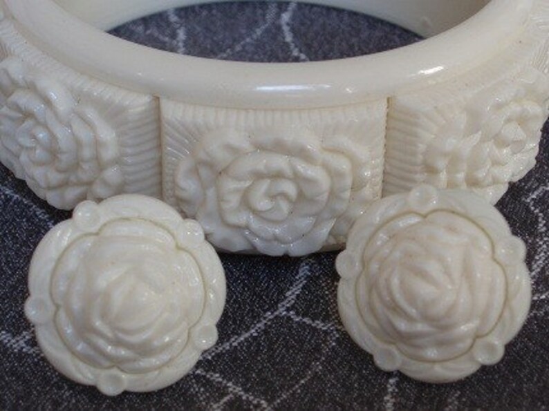 Pu&ograve; includere: Un set di orecchini e un braccialetto abbinati in plastica bianca scolpita. Gli orecchini e il braccialetto presentano un motivo a rosa in rilievo.