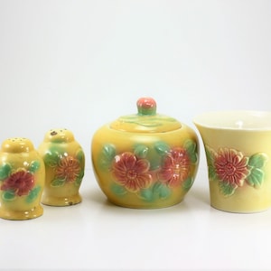 May include: A set of four vintage ceramic kitchenware pieces in a yellow and green floral pattern. The set includes a sugar bowl with a lid, two salt and pepper shakers, and a small vase.