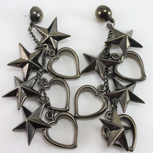 May include: A pair of dangle earrings with a silver finish. Each earring features a chain with multiple dangling stars and hearts.