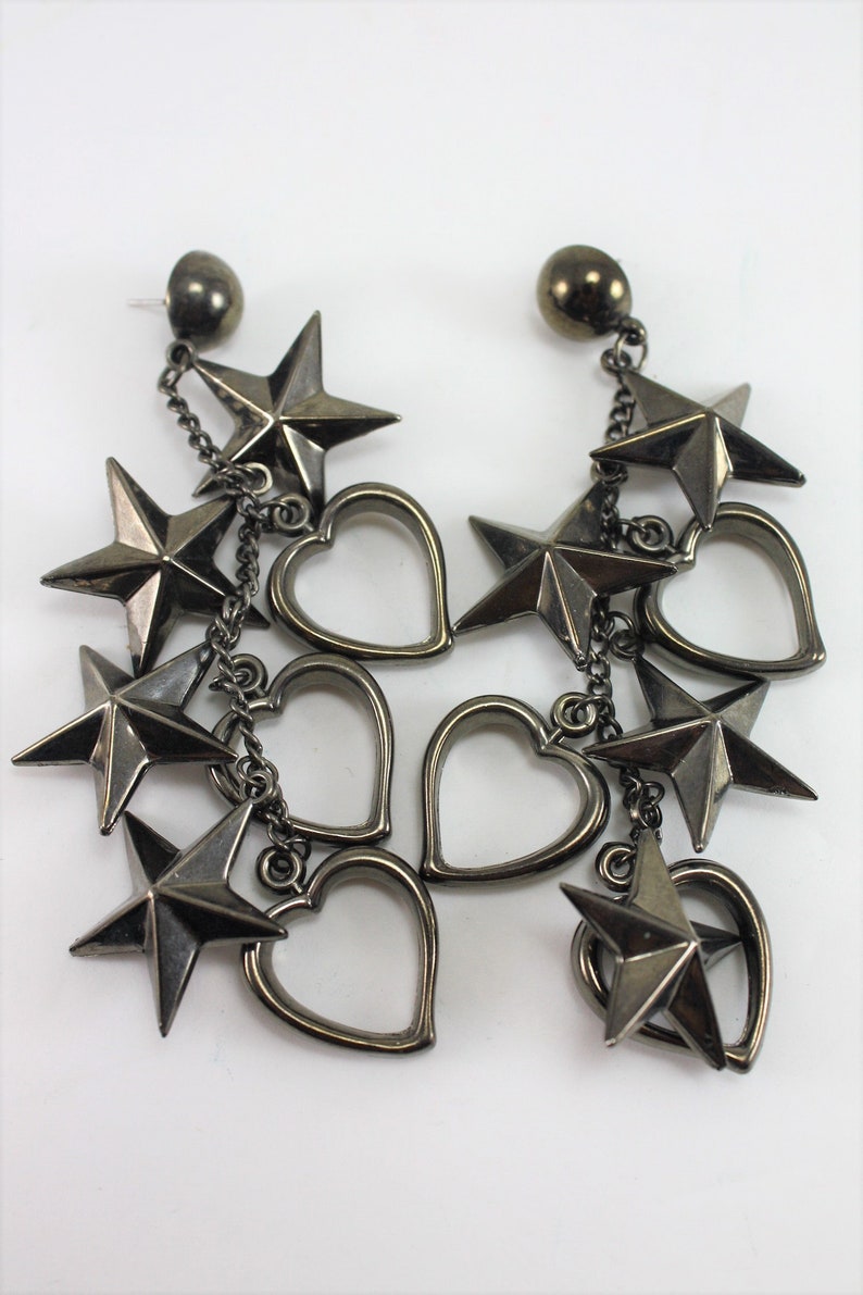May include: A pair of dangle earrings with a silver finish. Each earring features a chain with multiple dangling stars and hearts.